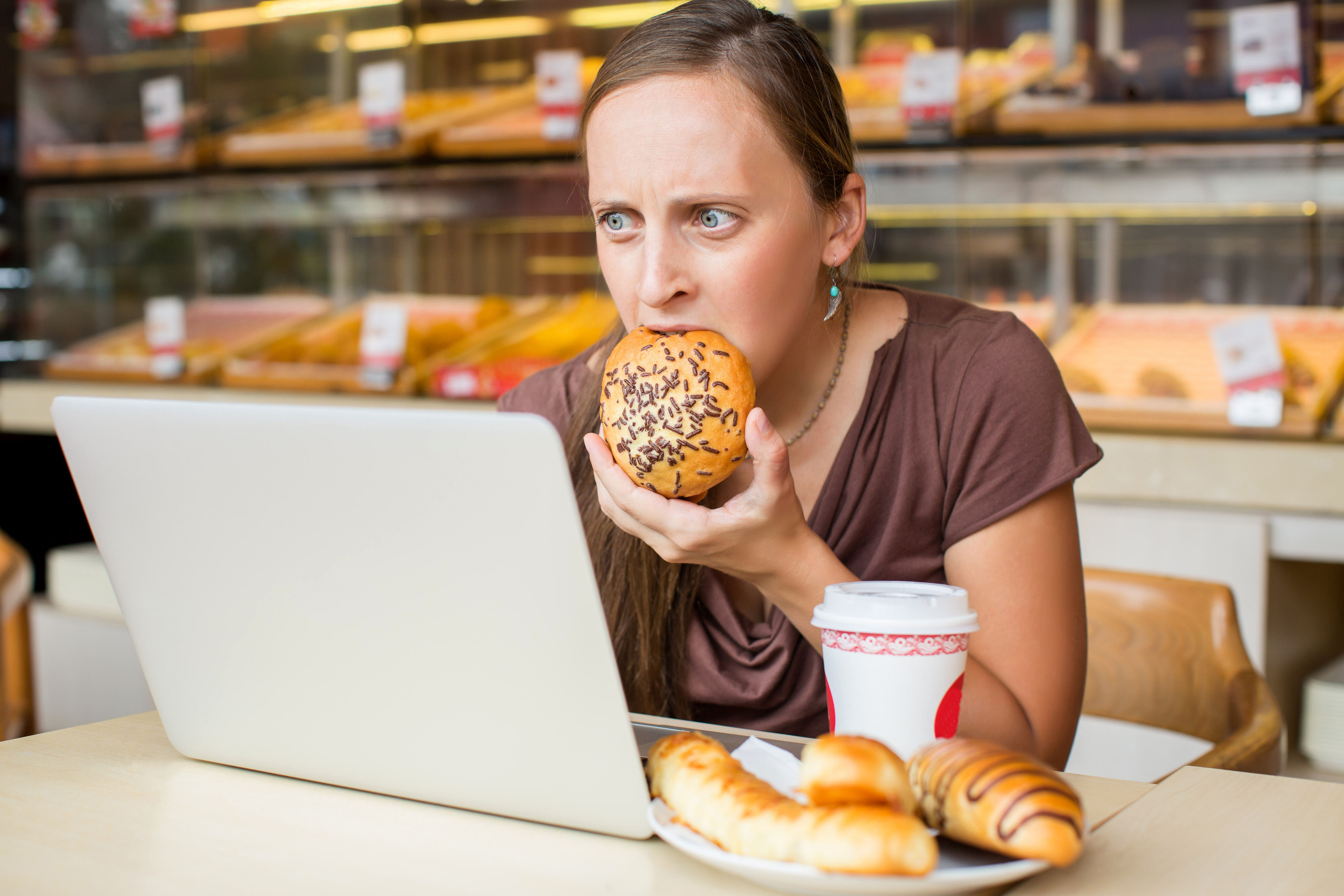 Frau sitzt am Notebook und beißt in ein weißes Brötchen